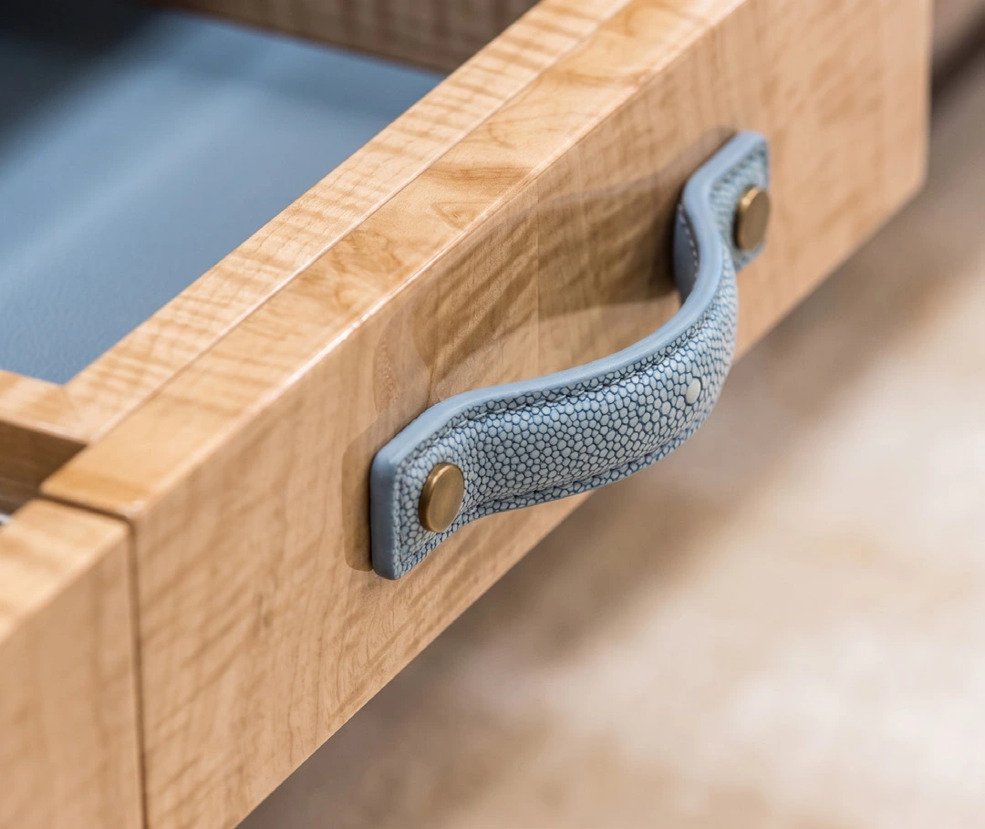 A blue textured handle with brass fixings on a figured timber drawer